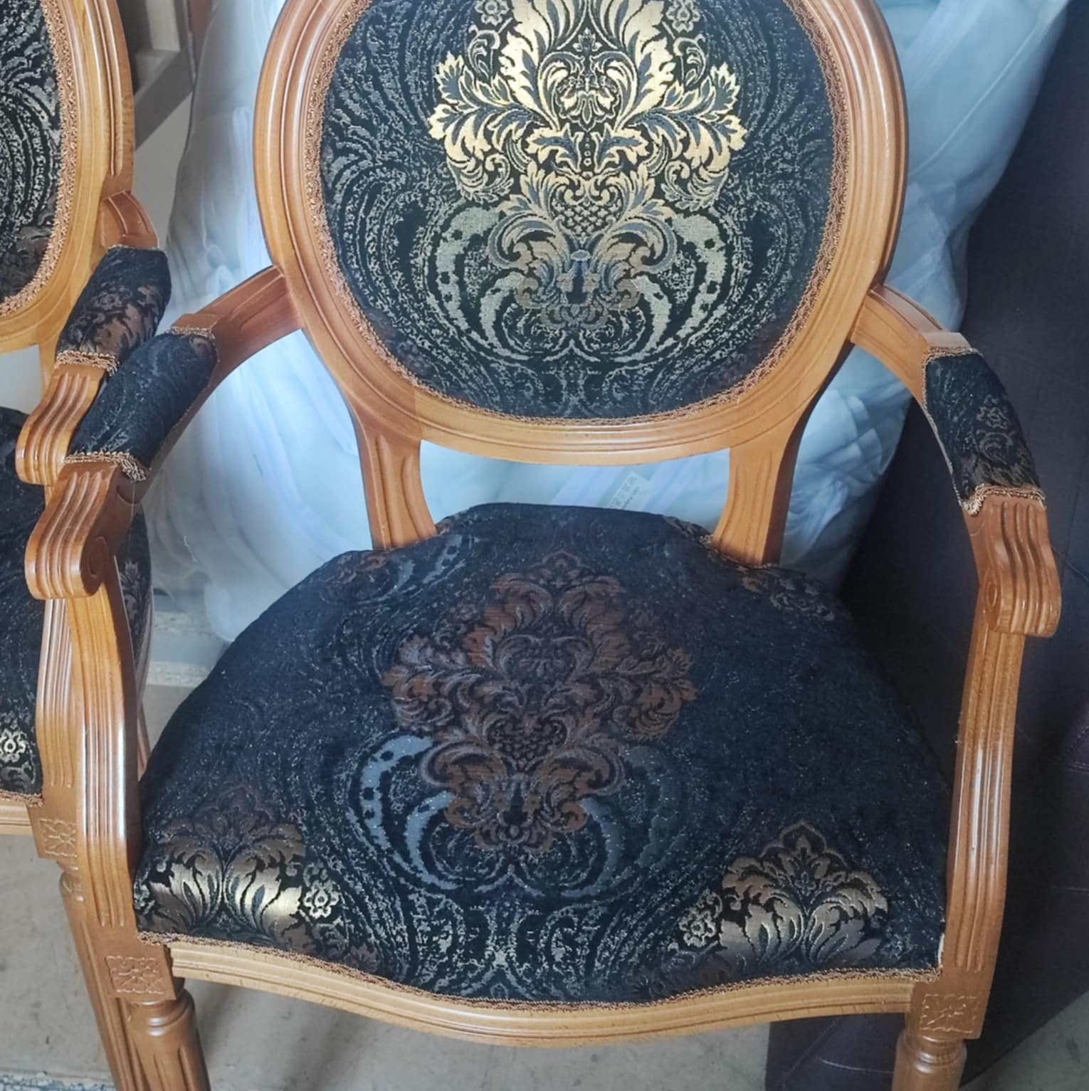 Dwa odnowione krzesła w stylu Ludwika z ciemną tapicerką w złote wzory. Krzesła mają drewniane, rzeźbione ramy i ozdobne wykończenia.