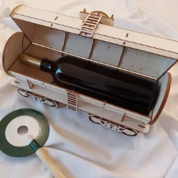 Drewniany wagonik z otwieraną klapą, zawierający butelkę wina, obok leży okrągły, zielono-biały podkładka pod kieliszek z drewnianą rączką, całość na białym tle.