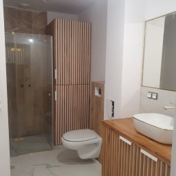 AllBud Usługi Ogólnobudowlane Łokietek Kamil - Nowoczesna łazienka z kabiną prysznicową, wiszącą toaletą i umywalką nablatową z drewnianą szafką w kolorze drewna z białymi akcentami.