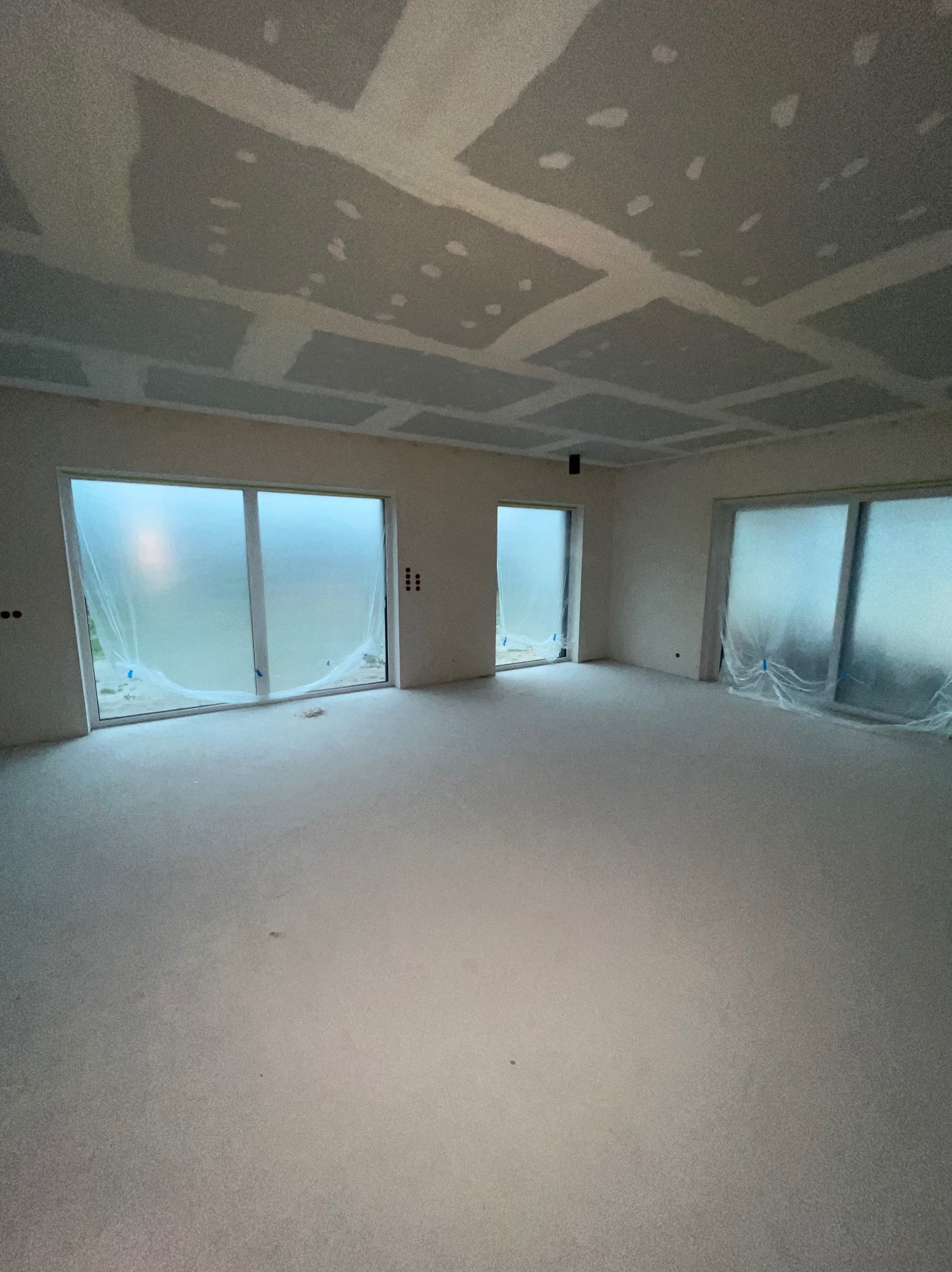 Wnętrze pokoju w trakcie remontu: sufit z płyt karton-gips, szpachlowane łączenia, okna zabezpieczone folią malarską, przygotowane do dalszych prac wykończeniowych.