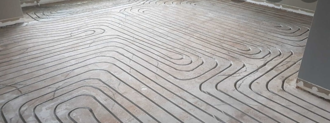 Wężykowa instalacja rur w szlichcie podłogowej, przygotowana do zalania wylewką samopoziomującą, widoczne fragmenty ścian.