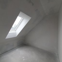 USŁUGI REMONTOWO-BUDOWLANE SOLIDFIX ARTUR FRANEK - Poddasze ze skośnym sufitem i oknem dachowym w trakcie prac wykończeniowych, widoczne ślady szpachlowania i przygotowania do malowania, surowy beton na podłodze.