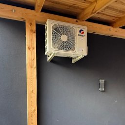 EcoPower+ Mateusz Kempiński - Klimatyzator marki Gree zamontowany na ścianie pod drewnianą konstrukcją dachu, widoczna lampa ścienna.