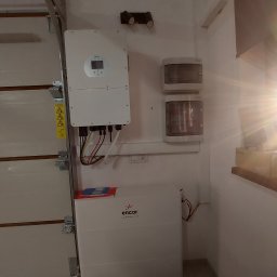 EcoPower+ Mateusz Kempiński - Zamontowany inwerter fotowoltaiczny i magazyn energii Encor w garażu, widoczne kable i zabezpieczenia elektryczne, obok brama garażowa.