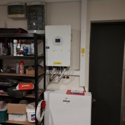 EcoPower+ Mateusz Kempiński - Biały inwerter Deye i magazyn energii Encor zamontowane na ścianie w pomieszczeniu gospodarczym, obok regału z różnymi przedmiotami i skrzynki elektryczne na górze.