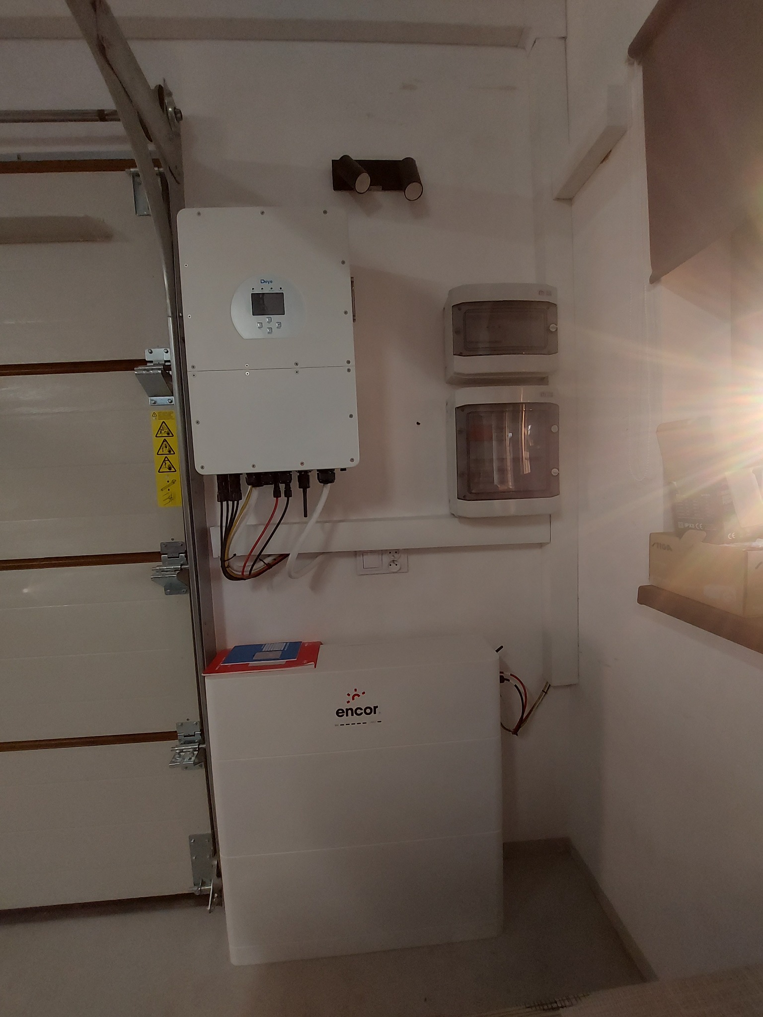 Zamontowany inwerter fotowoltaiczny i magazyn energii Encor w garażu, widoczne kable i zabezpieczenia elektryczne, obok brama garażowa.