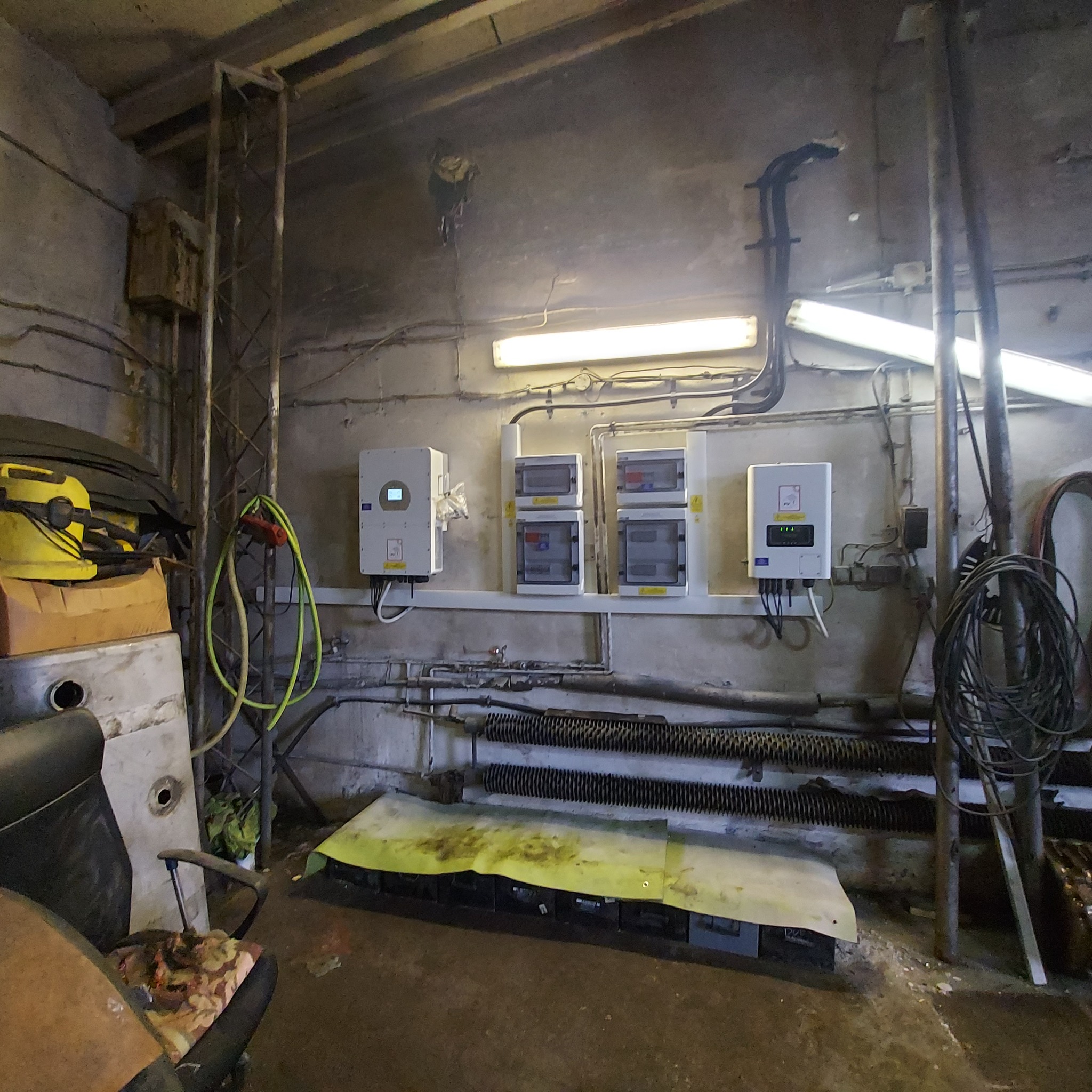 Piwnica z zamontowanymi inwerterami i rozdzielnicami elektrycznymi, widoczne rury instalacyjne, kable i skrzynka narzędziowa.