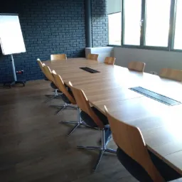 Nowoczesna sala konferencyjna z długim, jasnym stołem z drewna, otoczonym krzesłami na metalowych nogach, białą tablicą suchościeralną i ścianą z ciemnej cegły w tle, oświetlona przez okna z roletami.