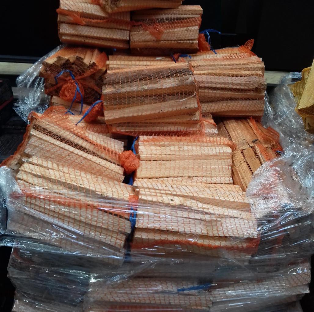 Ułożone pakiety drewna w siatkach z pomarańczowej siatki, zabezpieczone niebieskim sznurkiem, częściowo owinięte folią.