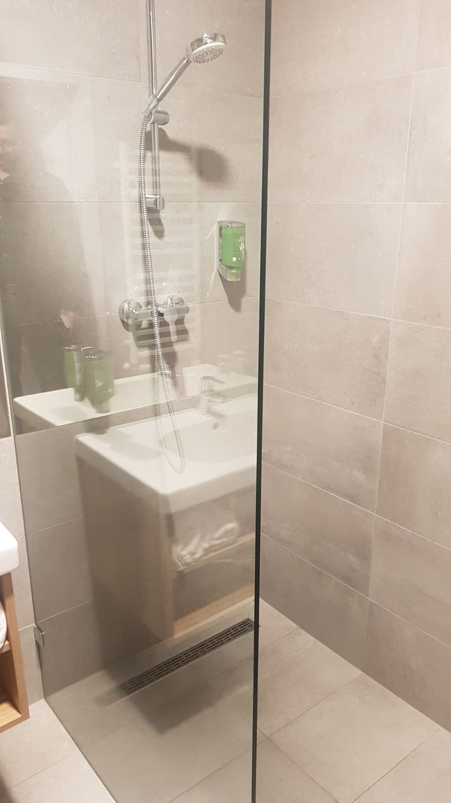 Nowoczesna łazienka z prysznicem typu walk-in, wykończona płytkami w odcieniach beżu, z widoczną szklaną kabiną, armaturą chromowaną i minimalistyczną umywalką z szafką.