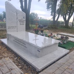 Kamieniarstwo Rakpol - Jasnoszary, nowoczesny nagrobek z wygrawerowanym tekstem i zdjęciem zmarłego, otoczony jesiennymi liśćmi na cmentarzu, z widocznym krzyżem w tle i osobą oddalającą się ścieżką.