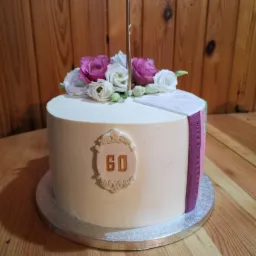 Tort urodzinowy na 60. rocznicę z dekoracją z żywych kwiatów i złotym numerem na beżowym tle.