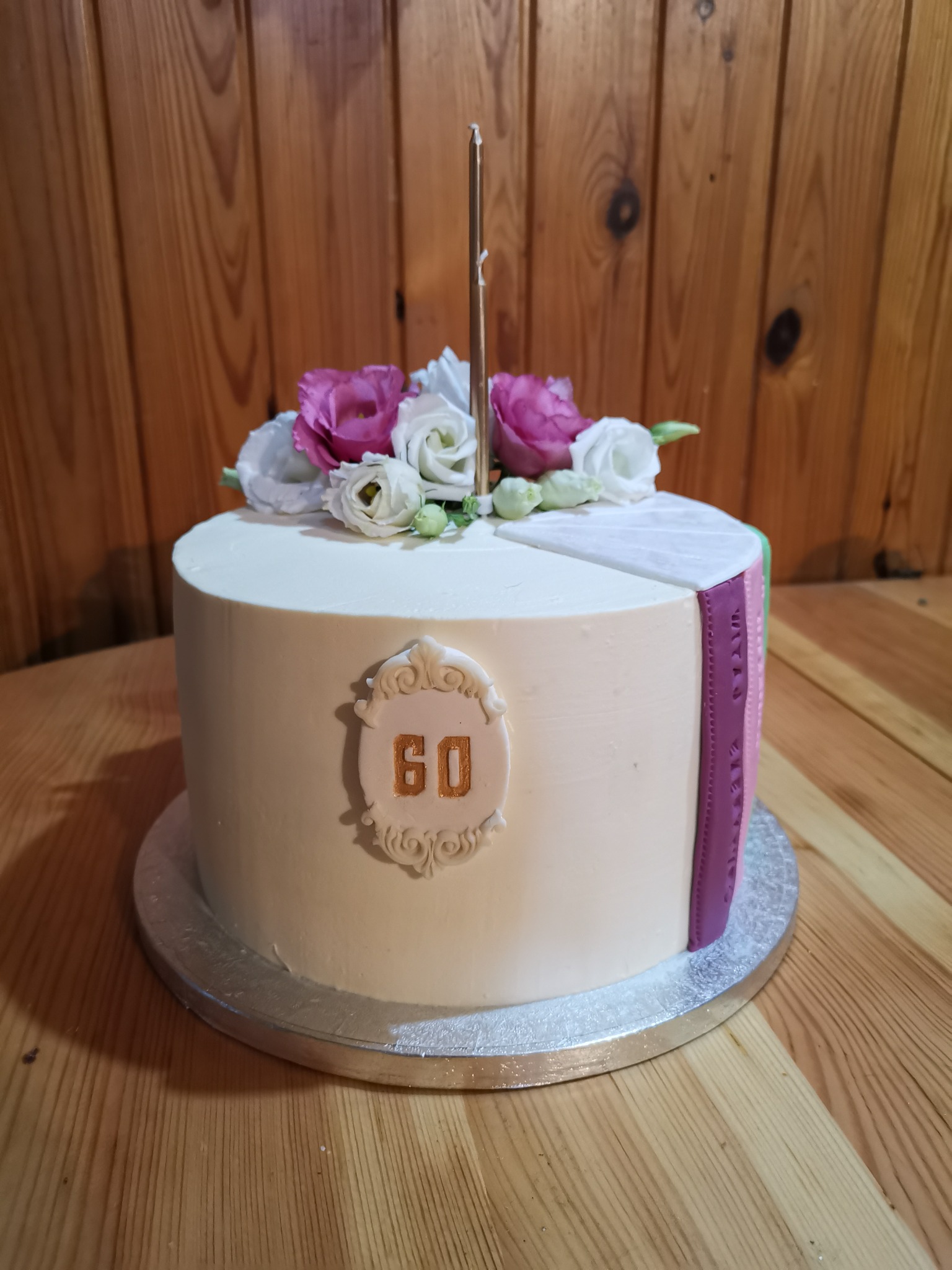 Tort urodzinowy na 60. rocznicę z dekoracją z żywych kwiatów i złotym numerem na beżowym tle.