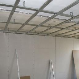 Remonty I Wykończenia Karol Szczęsny - Montaż sufitu podwieszanego z płyt karton-gips, widoczne metalowe profile i częściowo zamontowane płyty na ścianach, poziomica oparta o ścianę.