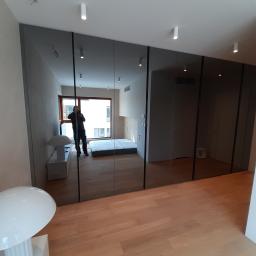 Remonty I Wykończenia Karol Szczęsny - Nowoczesna szafa wnękowa z przesuwnymi, lustrzanymi drzwiami w jasnym wnętrzu z drewnianą podłogą, widoczne odbicie osoby robiącej zdjęcie.