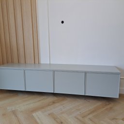 Remonty I Wykończenia Karol Szczęsny - Nowoczesna, szara szafka RTV z czterema frontami, zawieszona na ścianie z drewnianą boazerią i parkietem w jodełkę.