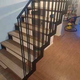 Remonty I Wykończenia Karol Szczęsny - Nowoczesne schody drewniane z czarną, metalową balustradą, widok z góry, w tle pokój dziecięcy z zabawkami i odkurzaczem.