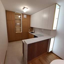 Remonty I Wykończenia Karol Szczęsny - Nowoczesna kuchnia z białymi szafkami wiszącymi, drewnianymi szafkami stojącymi, blatem z efektem marmuru i barkiem z drewnianymi lamelami.