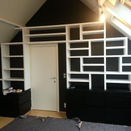 Remonty I Wykończenia Karol Szczęsny - Białe, asymetryczne półki na czarnym tle ściany, nad czarną komodą, w pokoju na poddaszu z oknem dachowym, fragment roboczej podłogi.