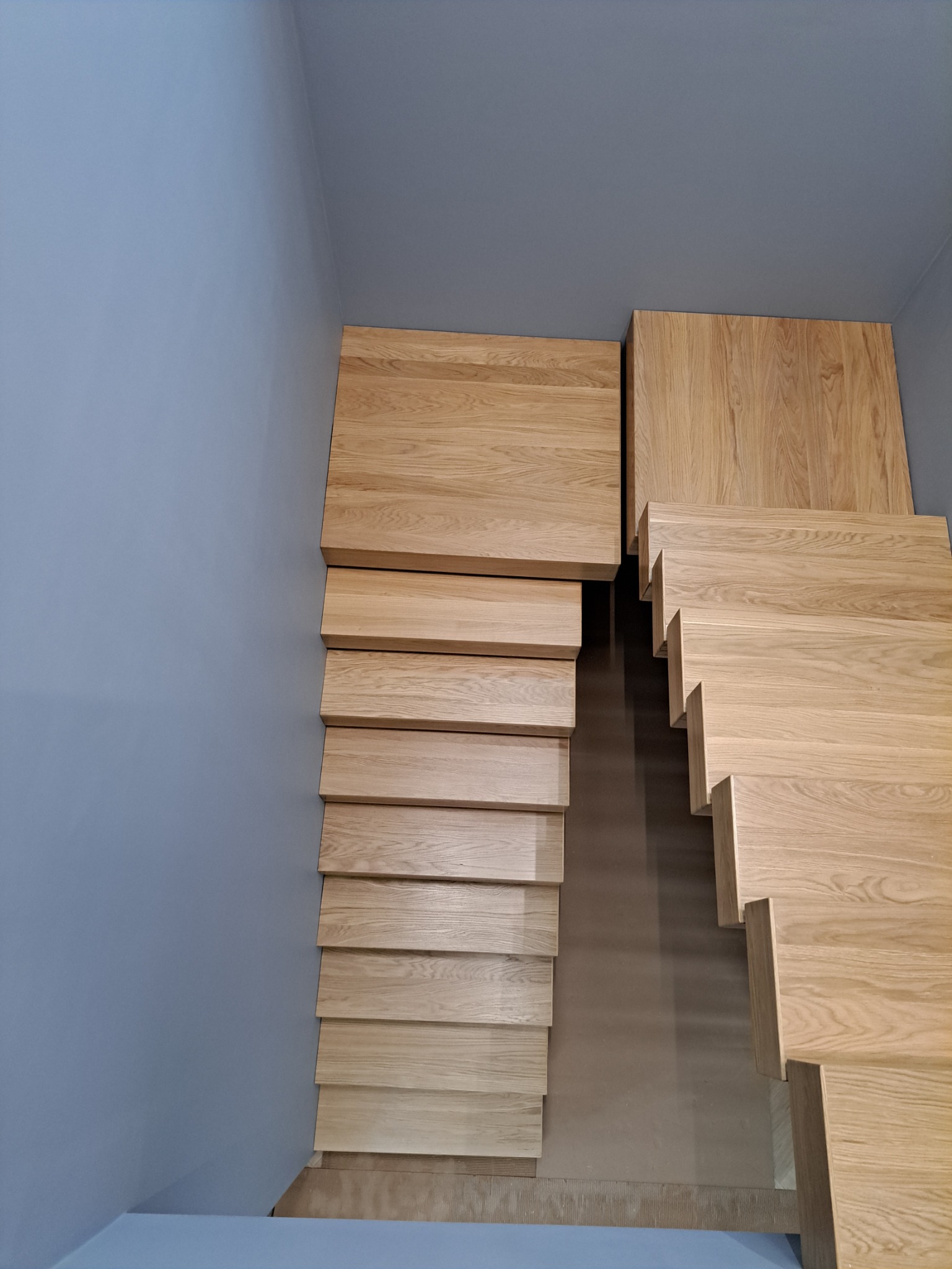 Nowoczesne, drewniane schody z jasnego drewna dębowego, z minimalistycznym designem, zamontowane przy szarej ścianie, widok z góry.