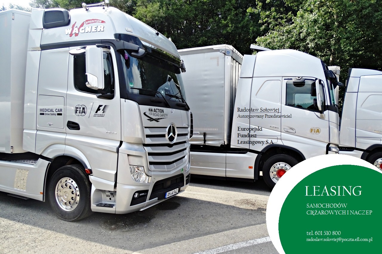 Srebrne ciągniki siodłowe z naczepami zaparkowane na placu, widoczne logo FIA i napisy 'MEDICAL CAR', 'FIA ACTION FOR ROAD SAFETY' oraz dane kontaktowe firmy leasingowej.