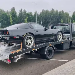 Czarna Corvette C4 na lawecie holowniczej z opuszczoną platformą najazdową na parkingu.