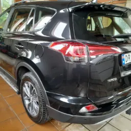 Błyszczący, czarny SUV Toyota RAV4 po myciu, widoczny z tyłu, z norweską tablicą rejestracyjną DR 59585, na tle wykafelkowanej ściany myjni.