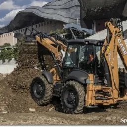 Żółto-czarna koparko-ładowarka CASE podczas prac ziemnych, wysypująca ziemię z łyżki na hałdę, w tle budynek o futurystycznej architekturze.