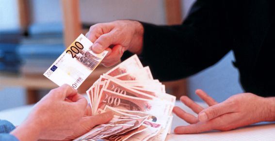 Przekazywanie pliku banknotów 200 euro z ręki do ręki, widoczne dłonie i część ubrań osób biorących udział w transakcji.