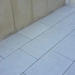 Ułożona szara kostka brukowa na tarasie, widoczne białe kamienie dekoracyjne wzdłuż ściany tarasu.