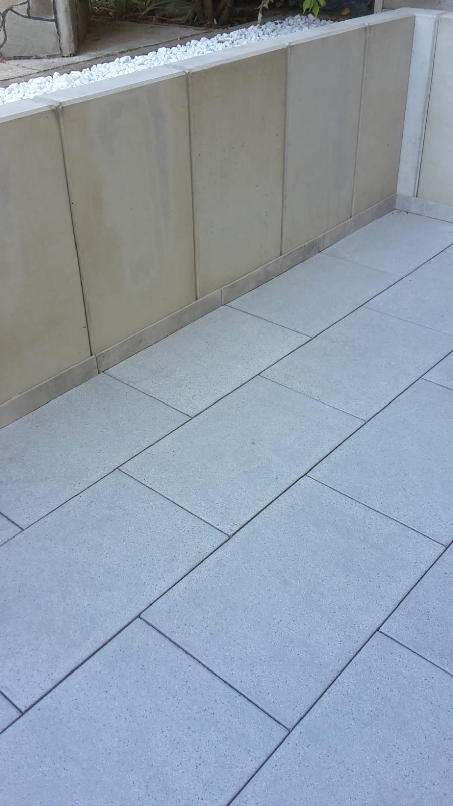 Ułożona szara kostka brukowa na tarasie, widoczne białe kamienie dekoracyjne wzdłuż ściany tarasu.