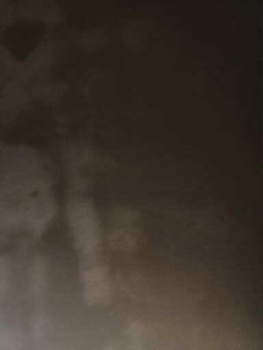 Świeżo nałożona, mokra warstwa szarego tynku na ścianie, widoczne zacieki i różnice w fakturze.