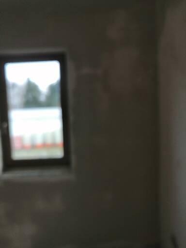 Ściana po szpachlowaniu, widoczne nierówności i okno z widokiem na zewnątrz.