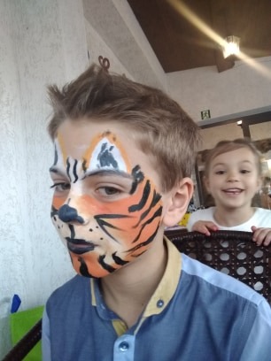 Chłopiec z pomalowaną twarzą w tygrysa, w tle uśmiechnięta dziewczynka.