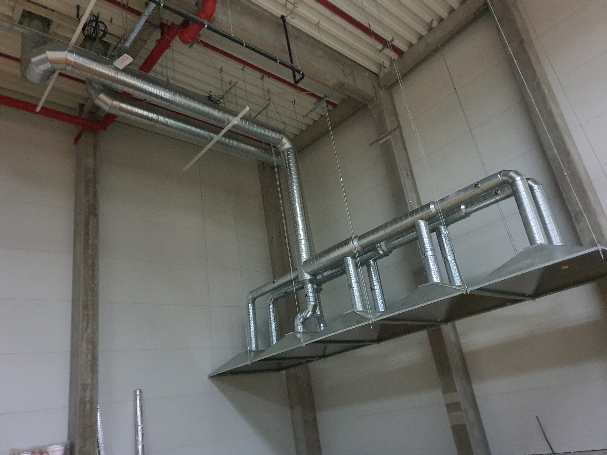 Kompleksowy system kanałów wentylacyjnych z metalu, zamontowany pod sufitem w hali przemysłowej, widoczne rury spiro i elementy mocujące.