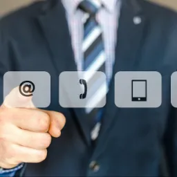 Mężczyzna w garniturze naciska palcem wirtualny przycisk z symbolem @, obok ikony telefonu, smartfona i koperty.