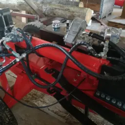 Czerwona, hydrauliczna łuparka do drewna z czarnymi przewodami hydraulicznymi, oponami i srebrnym zbiornikiem na płyn hydraulicznym.