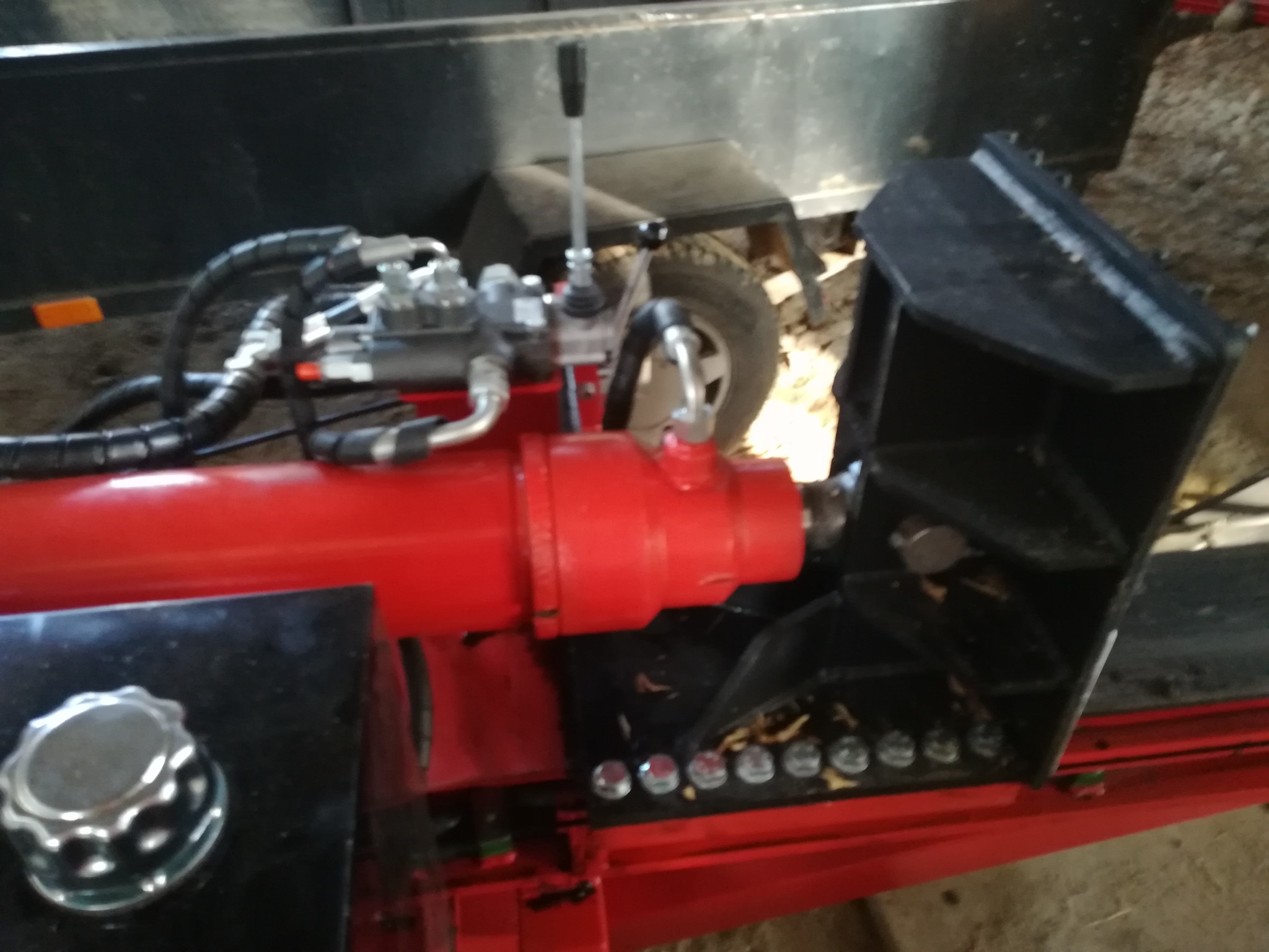 Widok z bliska czerwonej łuparki do drewna z hydraulicznym cylindrem i przewodami, stojącej na przyczepie.