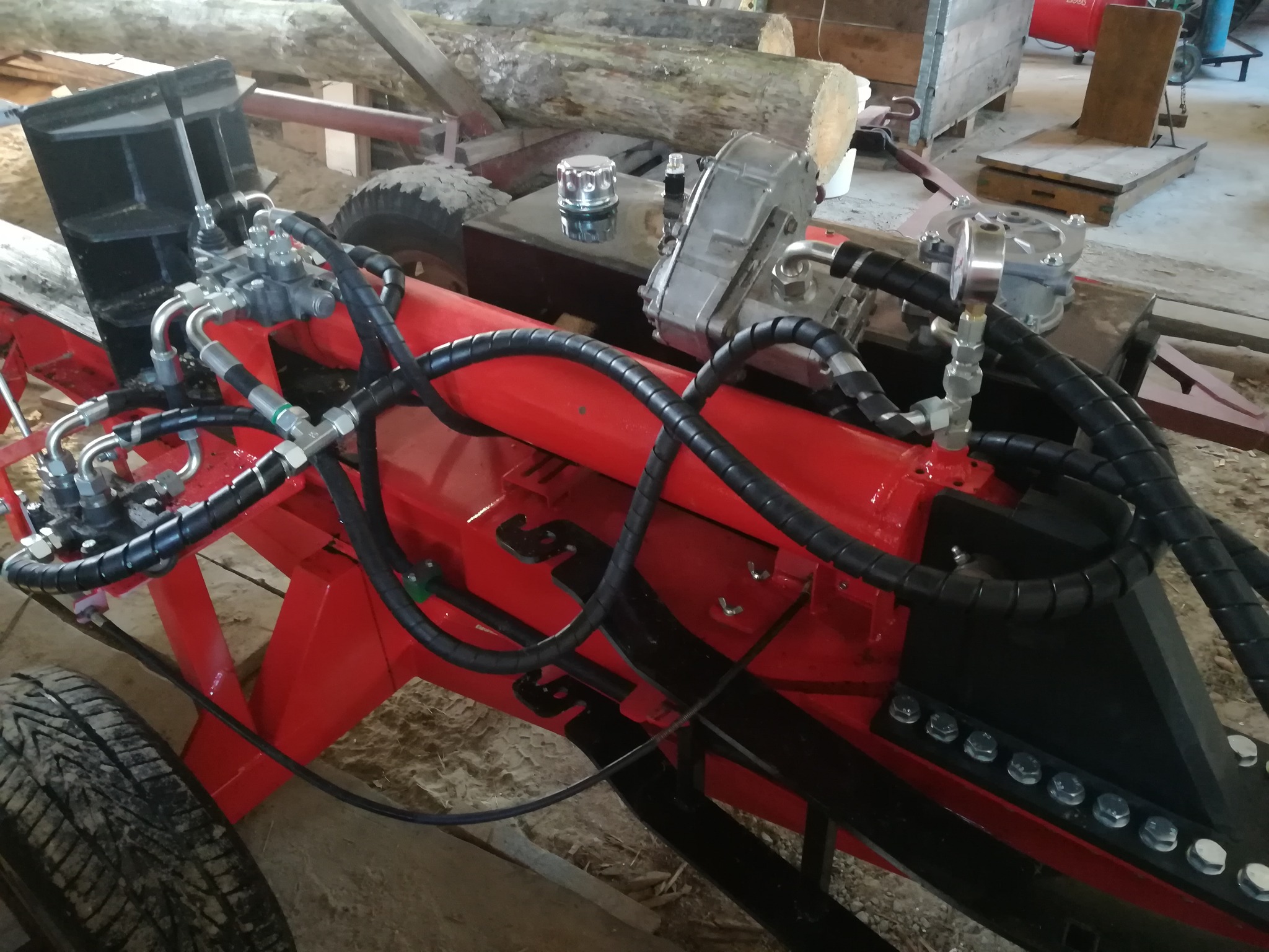 Czerwona, hydrauliczna łuparka do drewna z czarnymi przewodami hydraulicznymi, oponami i srebrnym zbiornikiem na płyn hydraulicznym.