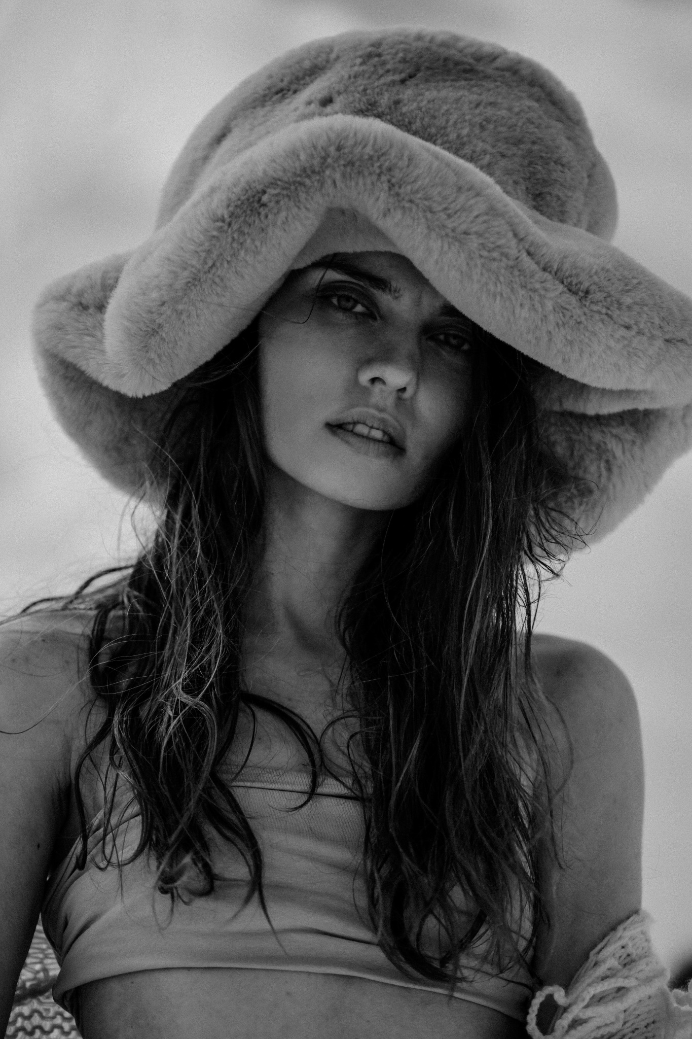 Portret kobiety w futrzanym kapeluszu, z mokrymi włosami, w czarno-białej tonacji, patrzącej w obiektyw.