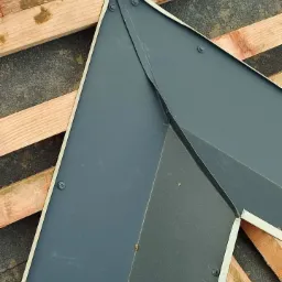 Szczegółowe ujęcie łączenia blacharskiego na dachu, widoczne śruby mocujące i drewniana konstrukcja pod spodem.