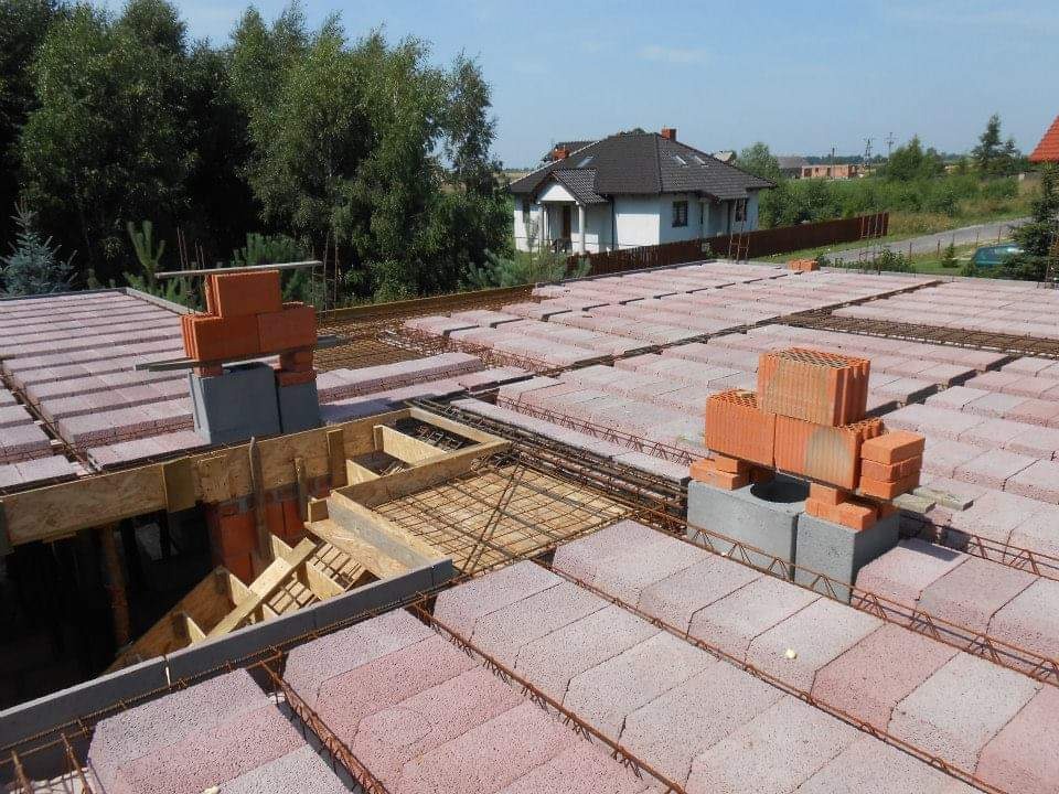 Wieniec stropowy z pustaków szalunkowych i zbrojenia, przygotowany do zalania betonem, widok z góry na budowę domu jednorodzinnego w słoneczny dzień.