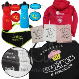 Różnorodne tekstylia z nadrukami: fartuchy kuchenne z motywem imbryka, czerwona kurtka z logo ARUA, ręczniki z napisem Soft, bandany sportowe i inne materiały z haftowanymi wzorami psów i napisami.