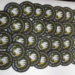 Kolekcja okrągłych naszywek wojskowych z wyhaftowanym białym orłem na zielonym tle i złotym napisem 'Klasa Przygotowania Wojskowego' oraz 'Bóg Honor Ojczyzna' z rokiem 2020, ułożonych na białej...