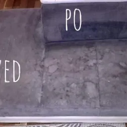 Szara tapicerka sofy z widoczną różnicą przed i po czyszczeniu, z napisem 'PRZED' na zabrudzonej części i 'PO' na czystej.