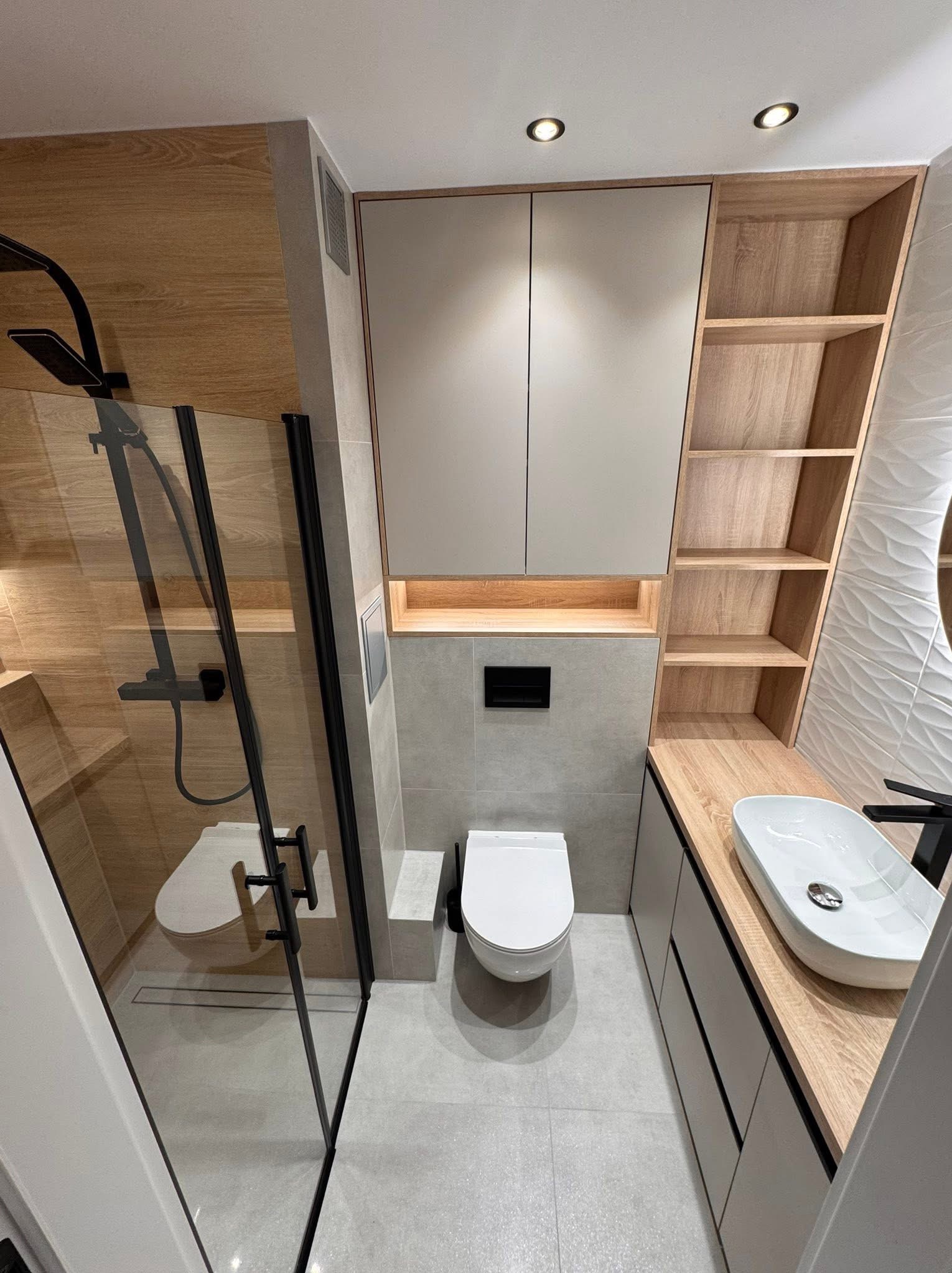 Nowoczesna łazienka z kabiną prysznicową typu walk-in, wiszącą toaletą i umywalką nablatową. Jasne drewno i szarość tworzą spójną całość. Minimalistyczny design.