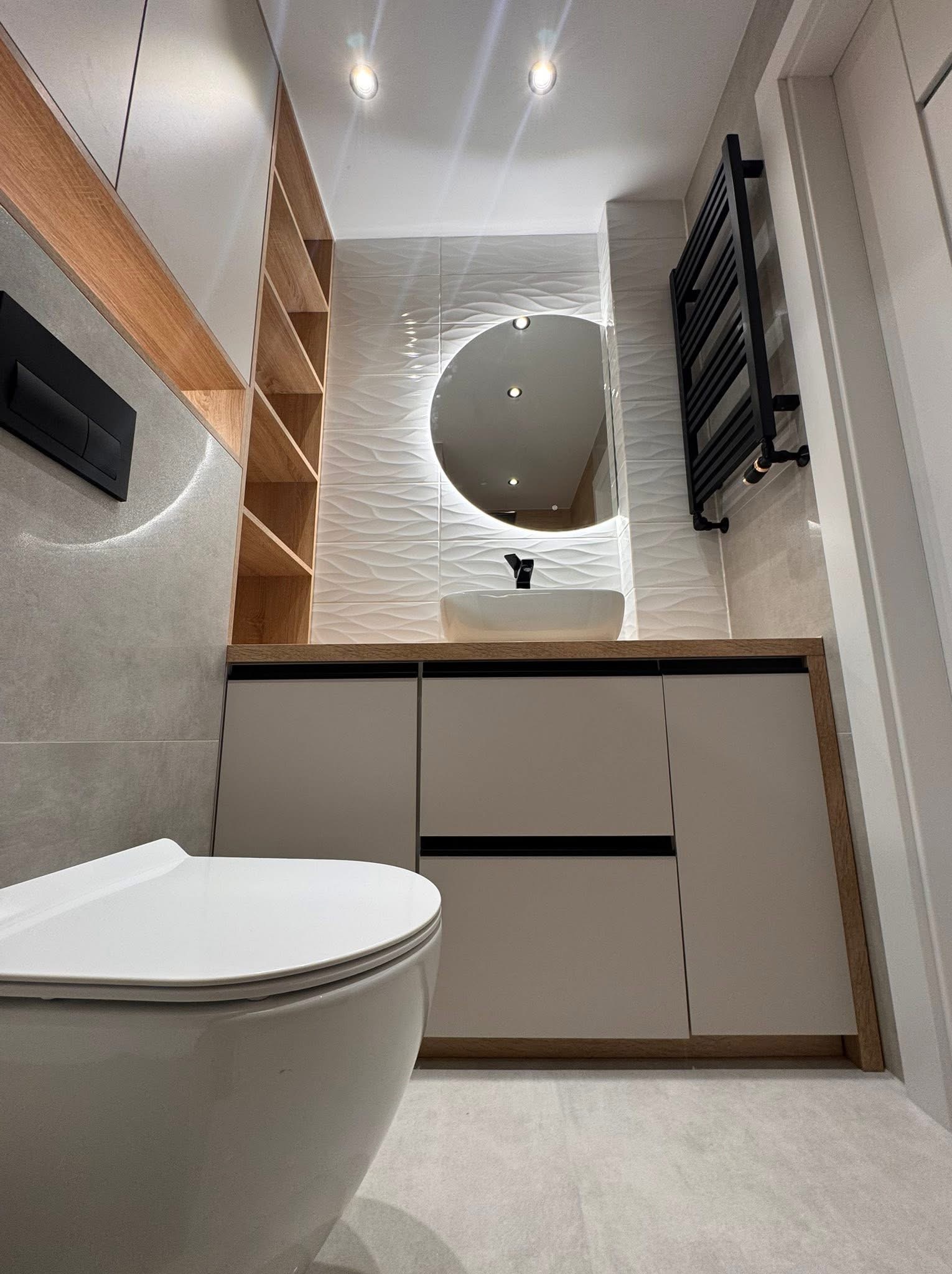 Nowoczesna łazienka z podświetlanym lustrem, umywalką nablatową i grzejnikiem drabinkowym. Jasne płytki z fakturą i drewniane akcenty. Ujęcie z dołu.