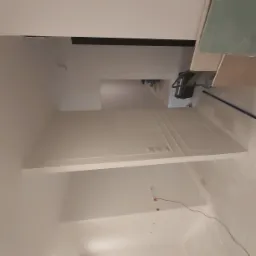 Wnętrze w trakcie prac wykończeniowych: białe ściany z dekoracyjnymi panelami, widoczne gniazdka elektryczne, narzędzia pracy w tle oraz płyta kartonowo-gipsowa przygotowana do montażu.