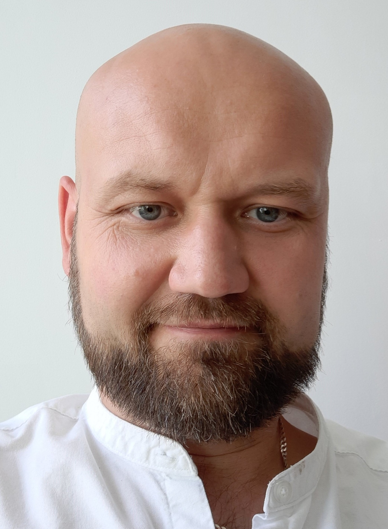 Portret brodatego mężczyzny z niebieskimi oczami w białej koszuli na jasnym tle, wykonany w Głogowie Małopolskim. Widoczny łańcuszek na szyi.