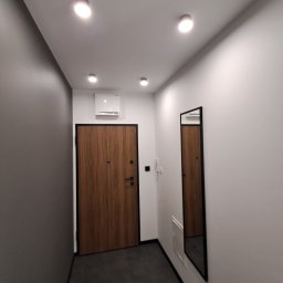 IDAO Ivan Hrynchuk - Nowoczesny przedpokój z drewnianymi drzwiami w czarnej ramie, szarą ścianą i minimalistycznym lustrem. Całość oświetlona punktowymi lampami sufitowymi.